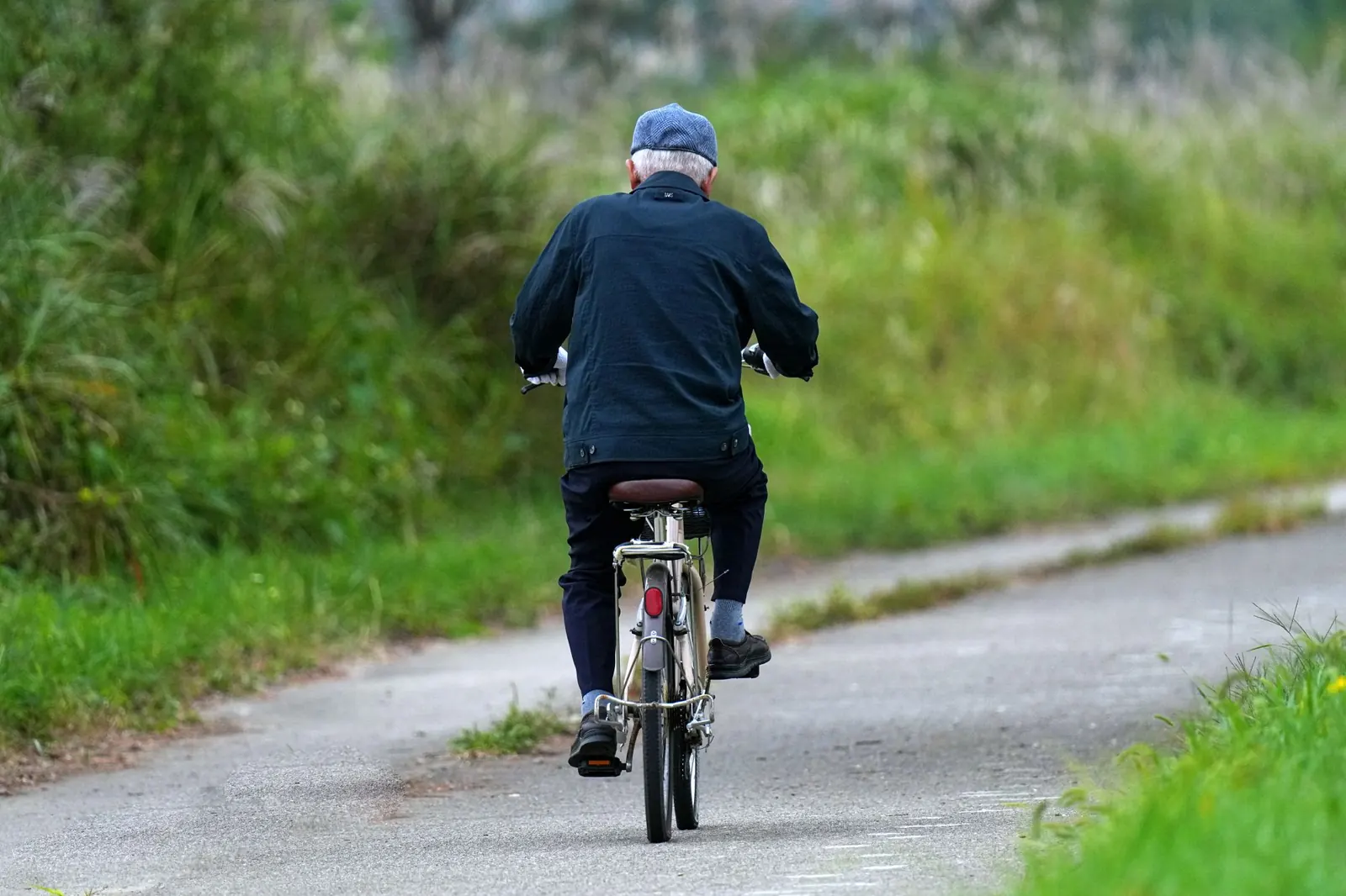 Older man cycling along a green countryside path